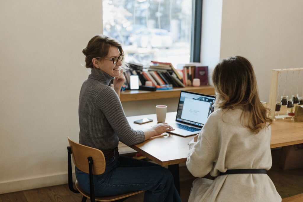 Two colleagues discussing their work beside a laptop in a bright office.